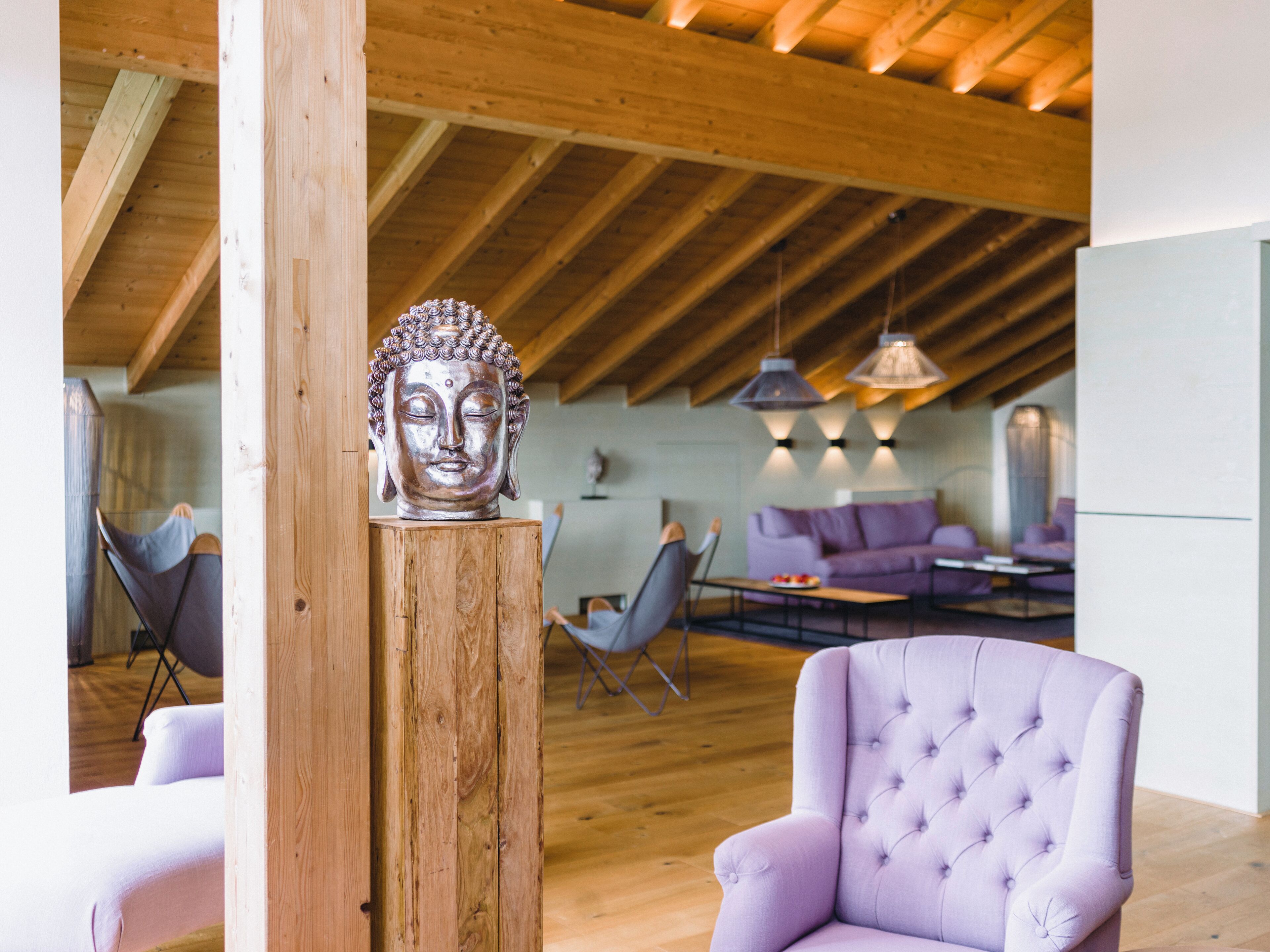 Un intérieur moderne avec un plafond en bois, une statue de Bouddha, un fauteuil violet et un coin repas comprenant un canapé et une table, tous deux de couleur violette.