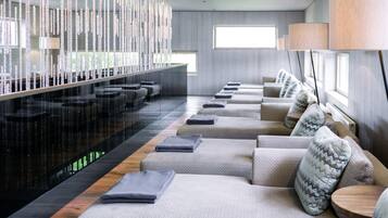 Un vestíbulo de hotel moderno con una hilera de sofás y sillones, una instalación de luces decorativa y amplias ventanas que dejan entrar la luz natural.