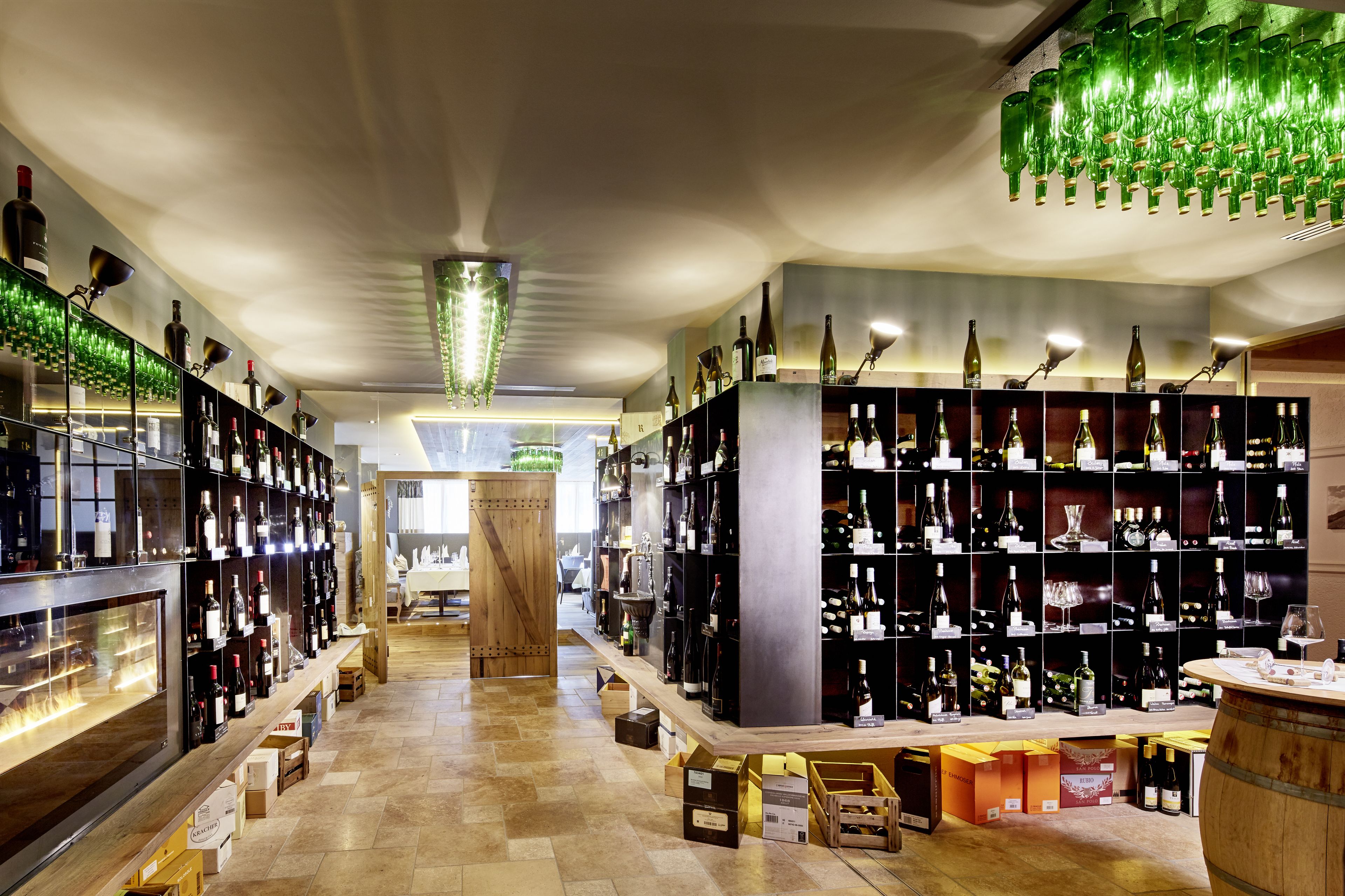 A wine cellar with shelves of wine bottles, wooden barrels, and a central wooden column.