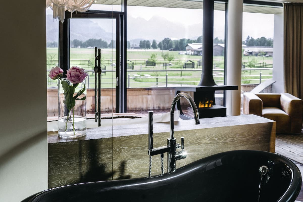 Une salle de bain moderne avec une grande fenêtre, une baignoire noire et un vase rempli de fleurs.