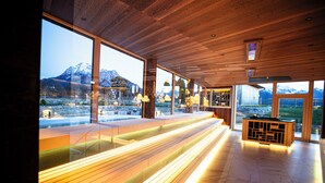 A modern interior with large windows, wooden benches, and a central seating area with a view of mountains. - Das König Ludwig - Adult Only (Schwangau)