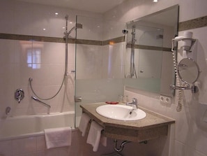 A modern bathroom with a glass-enclosed shower, a white sink, and a large mirror. - Hotel Tilmann Riemenschneider by ANS (Rothenburg ob der Tauber)