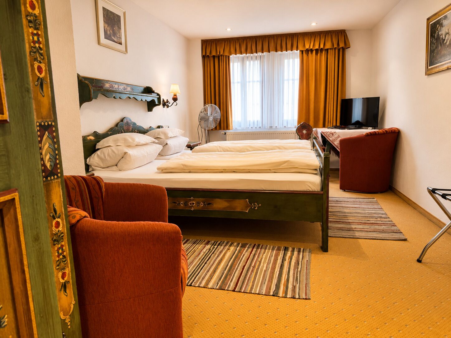Een hotelkamer met een bed, een stoel, een televisie en een raam met gordijnen.