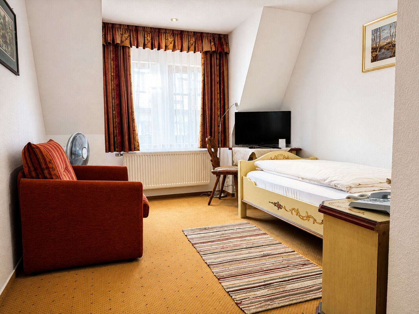 Habitación de hotel con cama, escritorio, silla, televisor y ventana con cortinas.