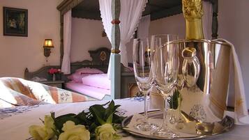 Un dormitorio con cama con dosel, una mesita de noche con lámpara y una bandeja con copas de champán y rosas.