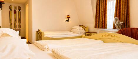 Une chambre d’hôtel avec deux lits, un coin salon avec un canapé, une fenêtre avec des rideaux et un ventilateur fixé au mur.
