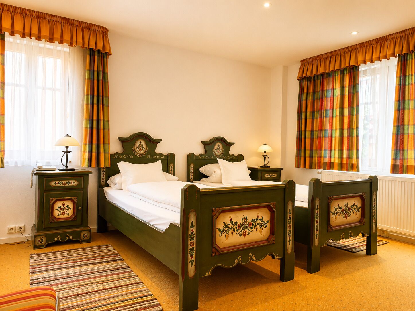 A traditional room with a double bed, two bedside tables with lamps, a patterned rug, and curtains.
