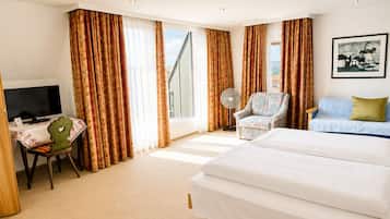 Een hotelkamer met een bed, een bureau met een televisie, een stoel, een bank en een raam met gordijnen.