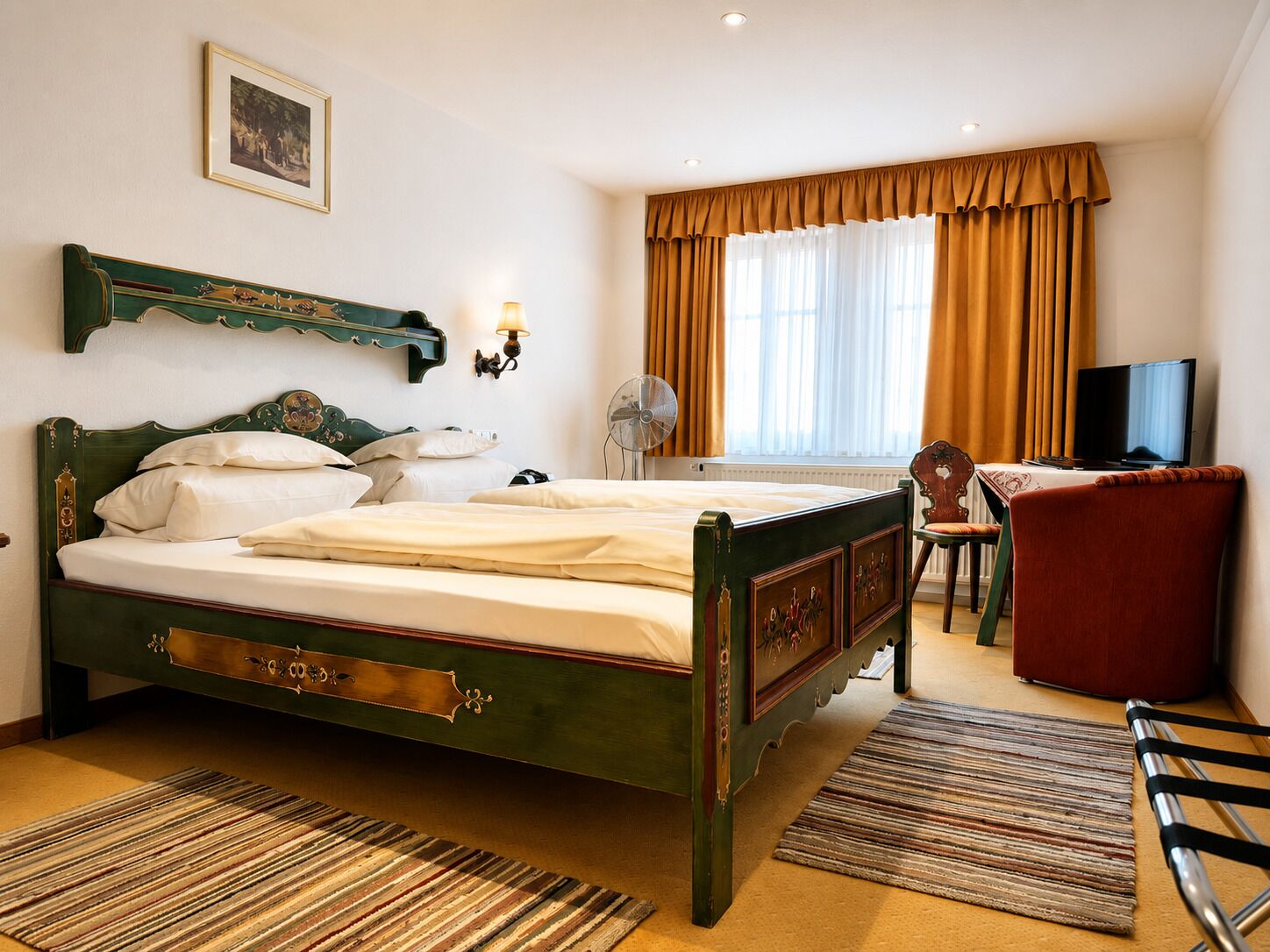 A hotel room with a large bed, a desk with a chair, a television, and a window with curtains.