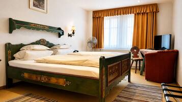 A hotel room with a large bed, a desk with a chair, a television, and a window with curtains.