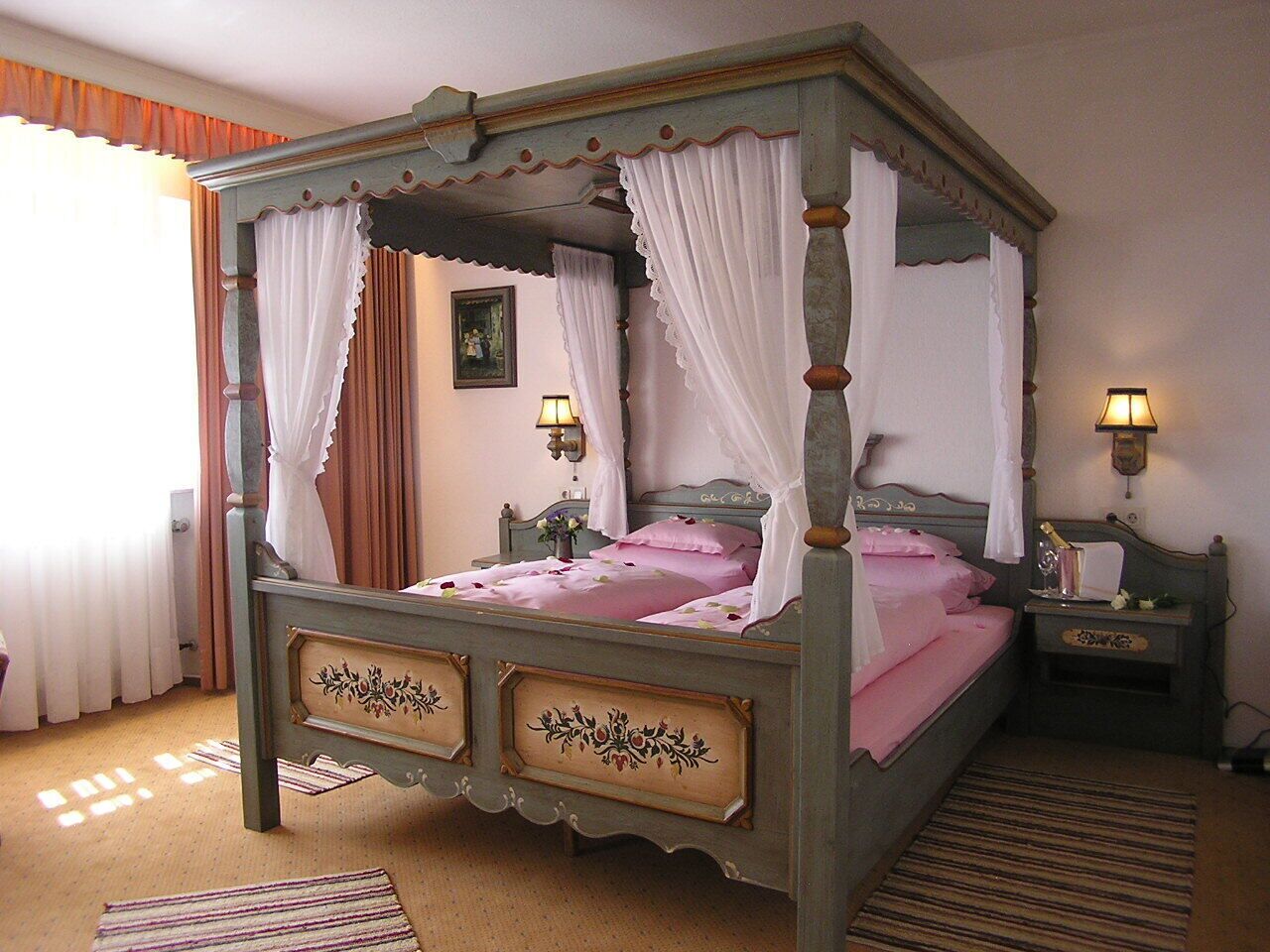 A four-poster bed with a canopy, a bedside table with a lamp, and a wall-mounted light fixture.