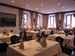 Un comedor con varias mesas, cada una con mantel, servilleta y cubiertos.