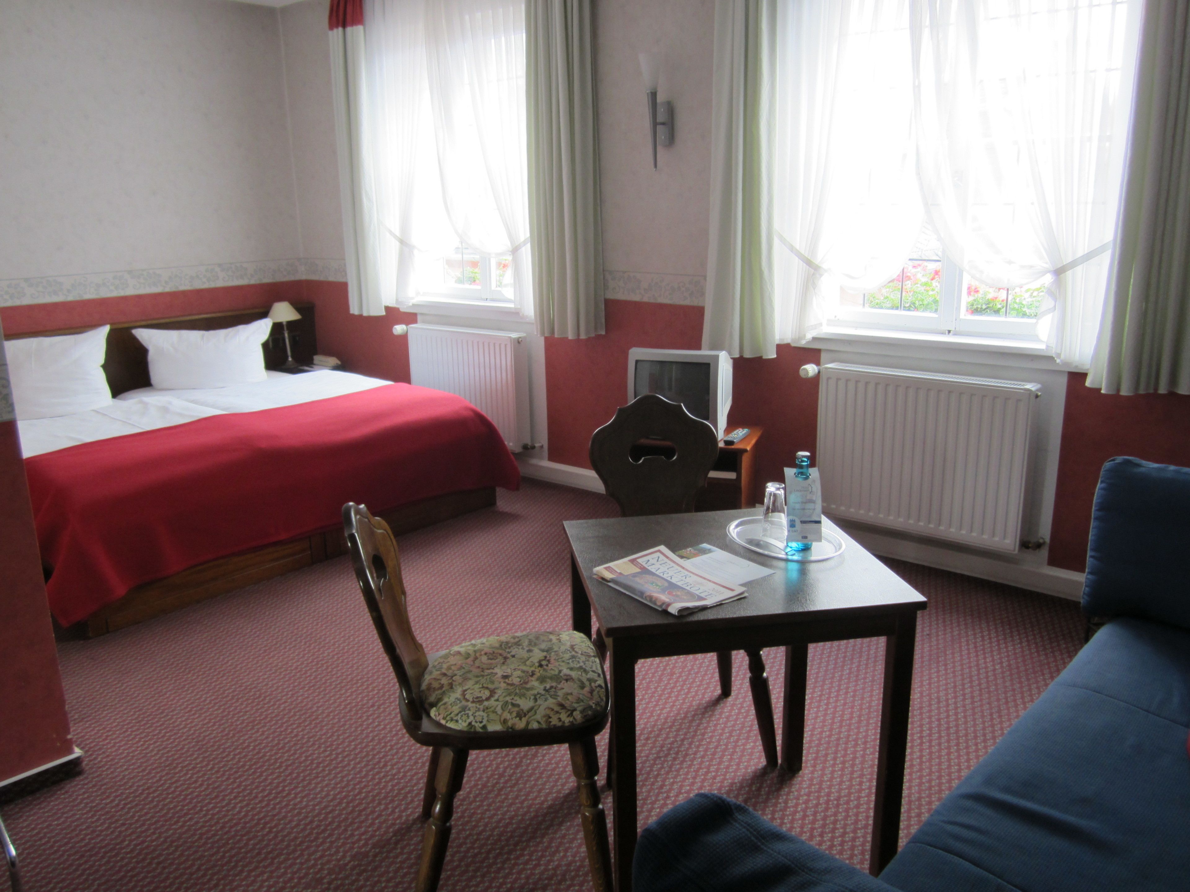 Ein Hotelzimmer mit Bett, Schreibtisch, Stuhl und einem Fenster mit Vorhängen.