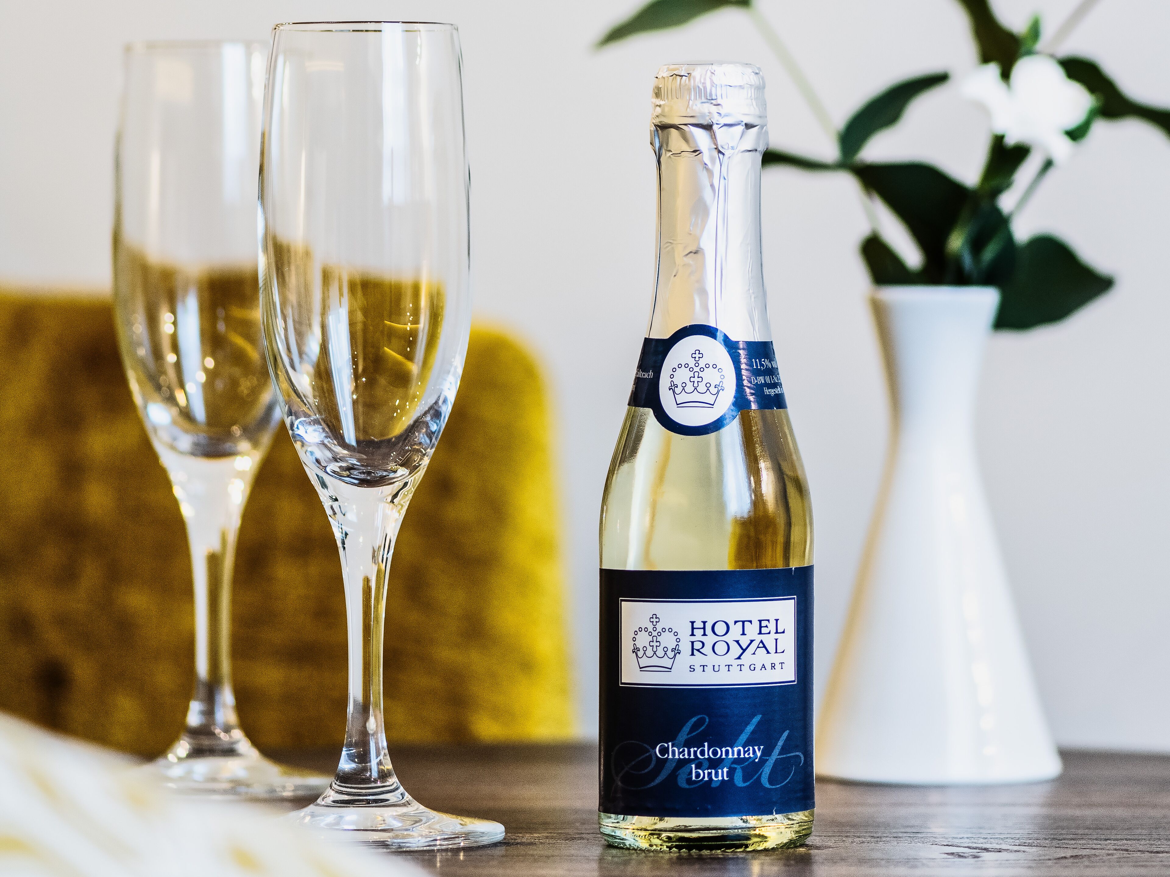 Una botella de Hotel Royal Stuttgärt Chardonnay Brut con dos copas de vino sobre una mesa.