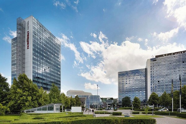 A modern hotel with a glass facade, surrounded by well-maintained greenery and other contemporary buildings. - Hotel Royal (Stuttgart)