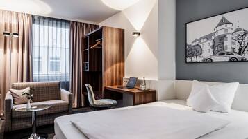 Una habitación de hotel con cama, escritorio, silla, mesita y armario.