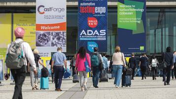 Un área exterior concurrida con pancartas para CastForge, la exposición de pruebas automotrices y SurfaceTechnology Germany.
