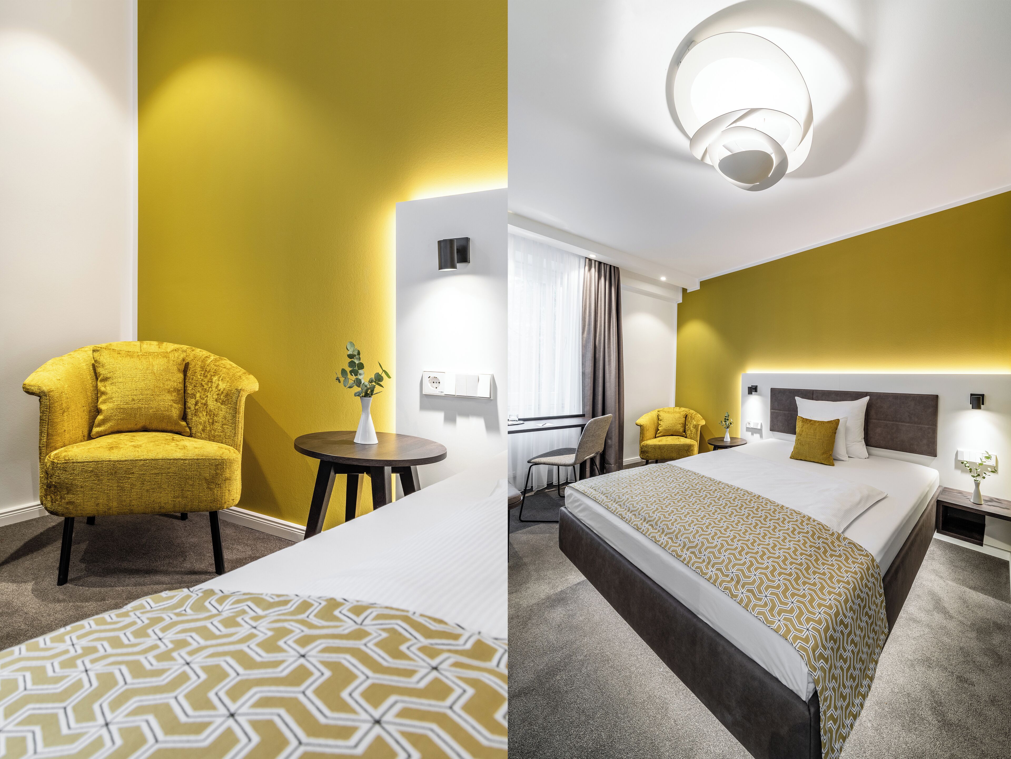 Ein Hotelzimmer mit gelber Akzentwand, einem runden Tisch mit Blumenvase, einem Bett mit gemustertem Überwurf und einer modernen Deckenleuchte.