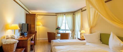A hotel room with a bed, two bedside tables with lamps, a desk with a television, a chair, and a window with curtains.