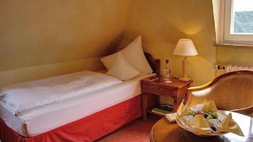 Habitación de hotel con una cama individual, una mesita de noche con lámpara, una silla y una cesta de frutas.