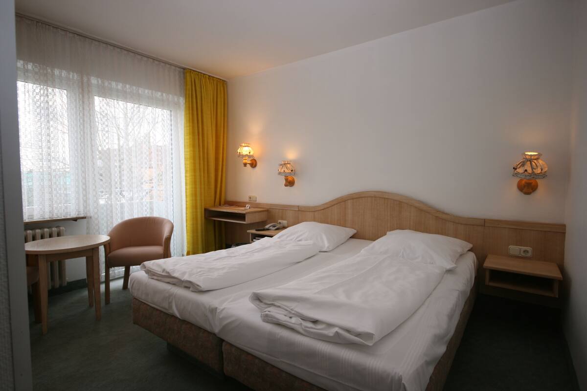 A hotel room with two beds, a chair, a table, and two bedside lamps.