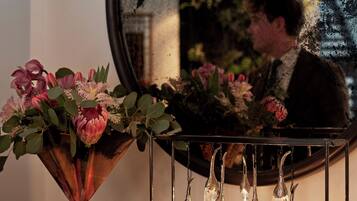 A wooden console table with a vase of flowers and a mirror reflecting a person.