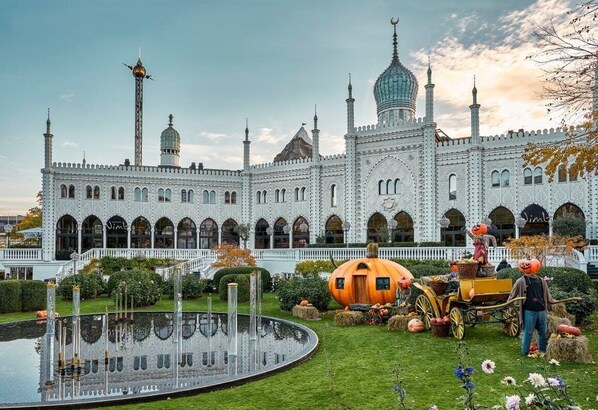 A large, ornate building with multiple towers and domes, surrounded by a well-maintained garden with a fountain and autumn decorations. - Nimb Hotel (Copenhagen)