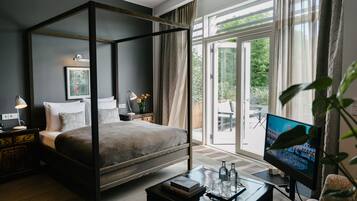 A modern bedroom with a four-poster bed, a television, and a view of the outdoors.