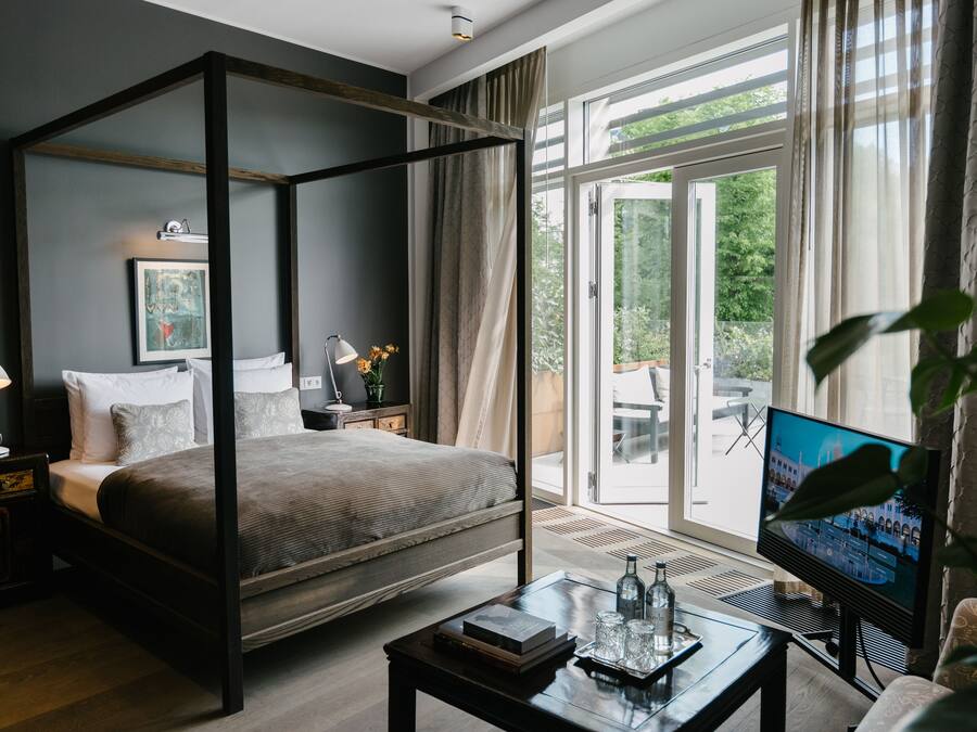 A modern bedroom with a four-poster bed, a television, and a view of the outdoors.