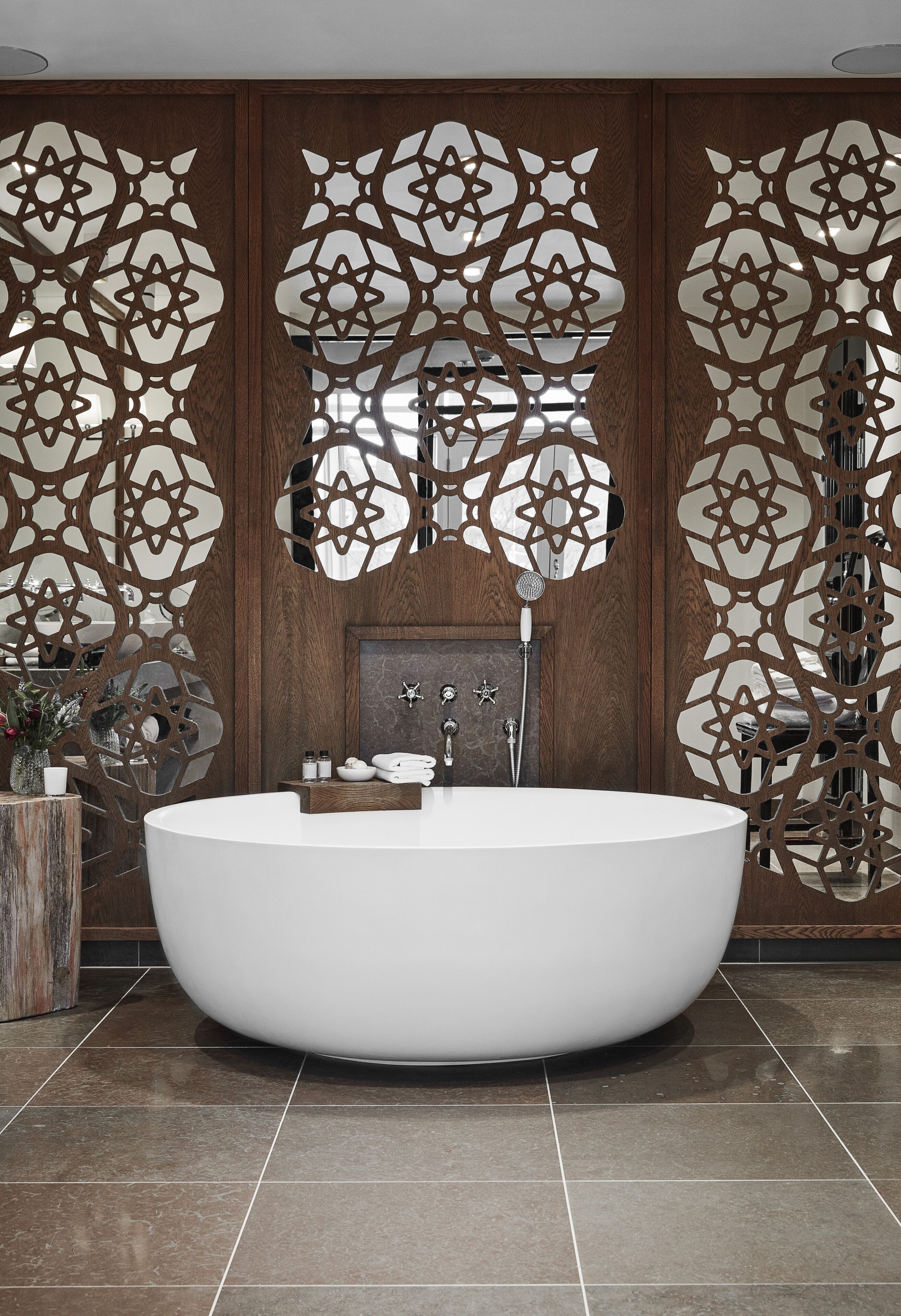 Un baño moderno con una bañera independiente, paneles de madera con diseños intrincados y una encimera de mármol.