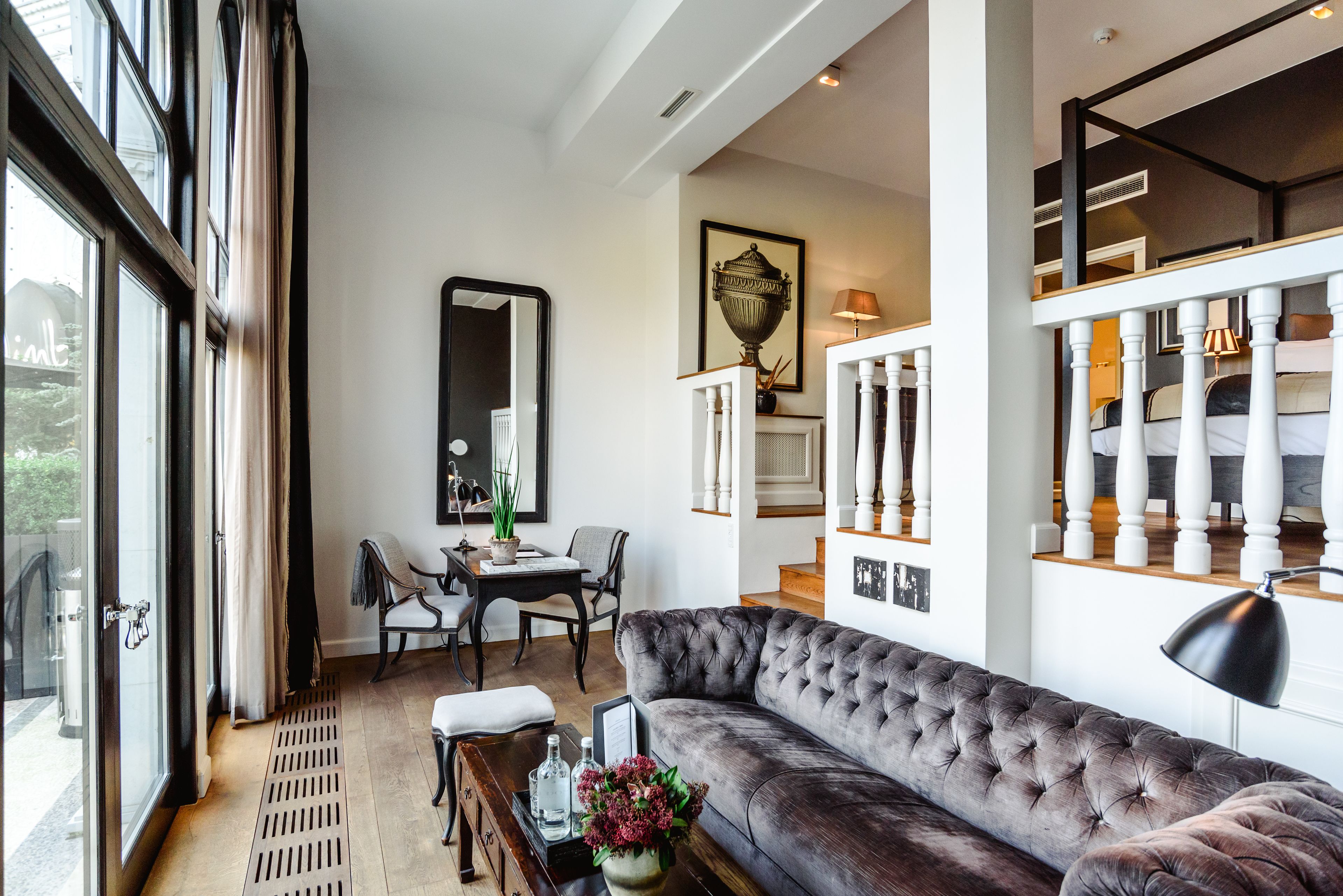 A modern living room with a large window, a sofa, a dining table, and a staircase.