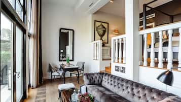 A modern living room with a large window, a sofa, a dining table, and a staircase.
