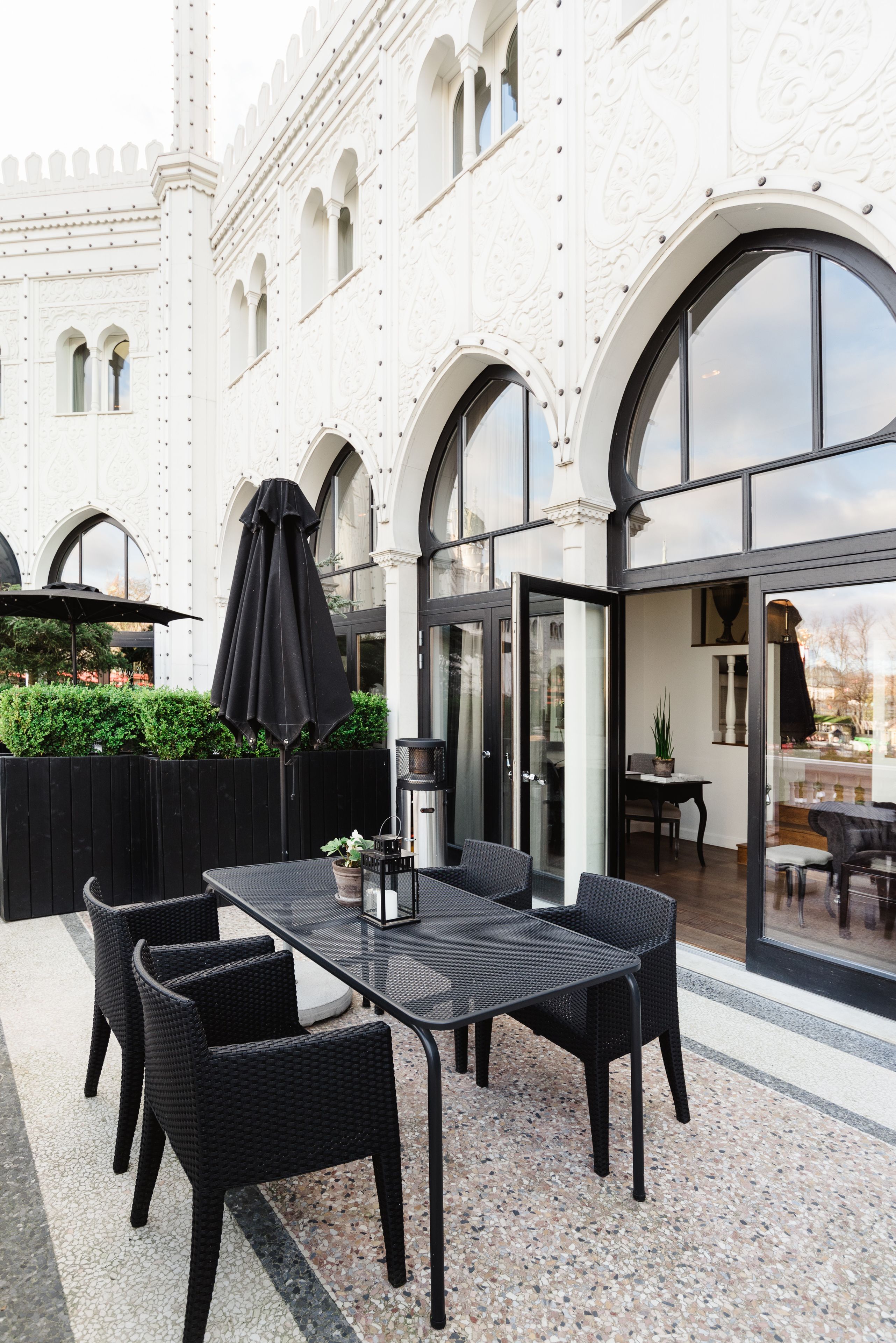 An outdoor patio with a table and chairs, a black umbrella, and a glass door leading to an interior space.