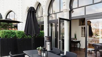 An outdoor patio with a table and chairs, a black umbrella, and a glass door leading to an interior space.