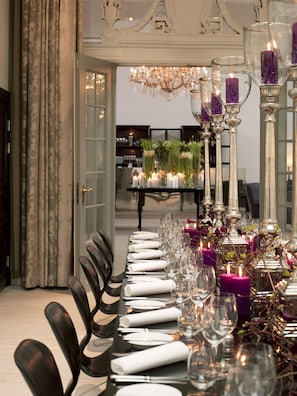 A formal dining table set with white napkins, silverware, and glassware, adorned with purple candles and greenery.