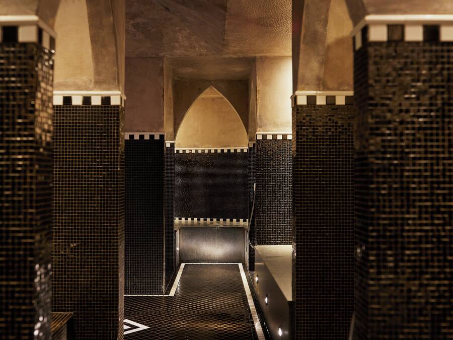 Un baño moderno con mosaicos blanco y negro, un nicho central en arco y un suelo reflectante.