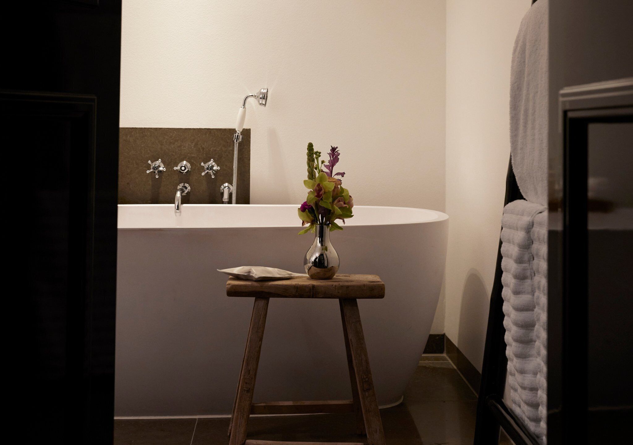 Un baño con una bañera independiente, un taburete de madera con un florero y un perchero.