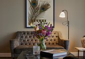 A tufted sofa, a vase with flowers, a lamp, and a book on a table.
