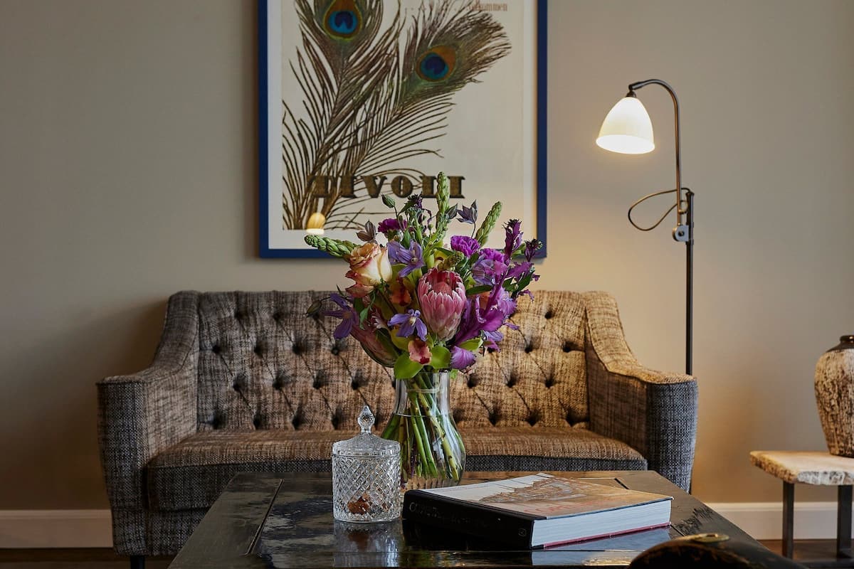 A tufted sofa, a vase with flowers, a lamp, and a book on a table.