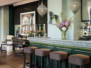 A bar area with green bar stools, a decorative mirror, and a vase of flowers.
