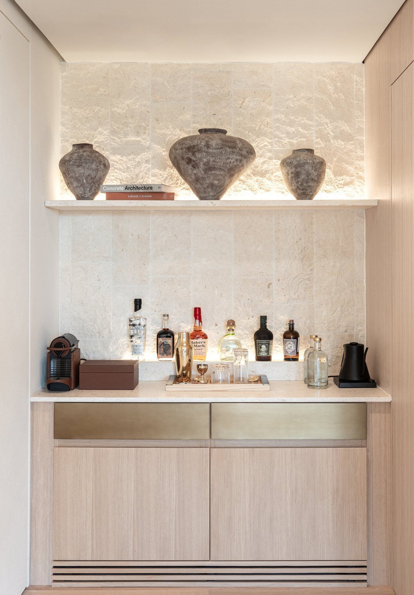 A kitchen with a marble backsplash, a shelf with decorative vases, and a variety of bottles on the counter.
