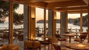 Un restaurant doté de grandes fenêtres offrant une vue sur la côte, avec des tables et des chaises disposées pour accueillir les clients.