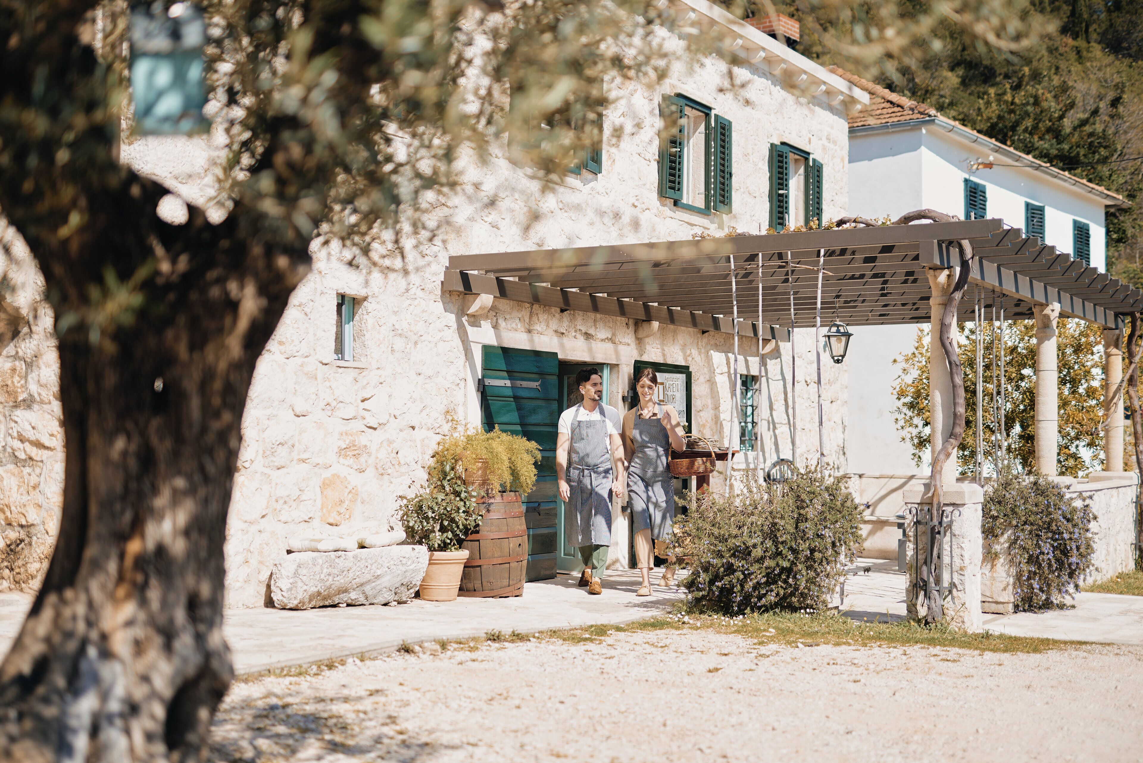 A rustic stone building with a wooden pergola and potted plants.