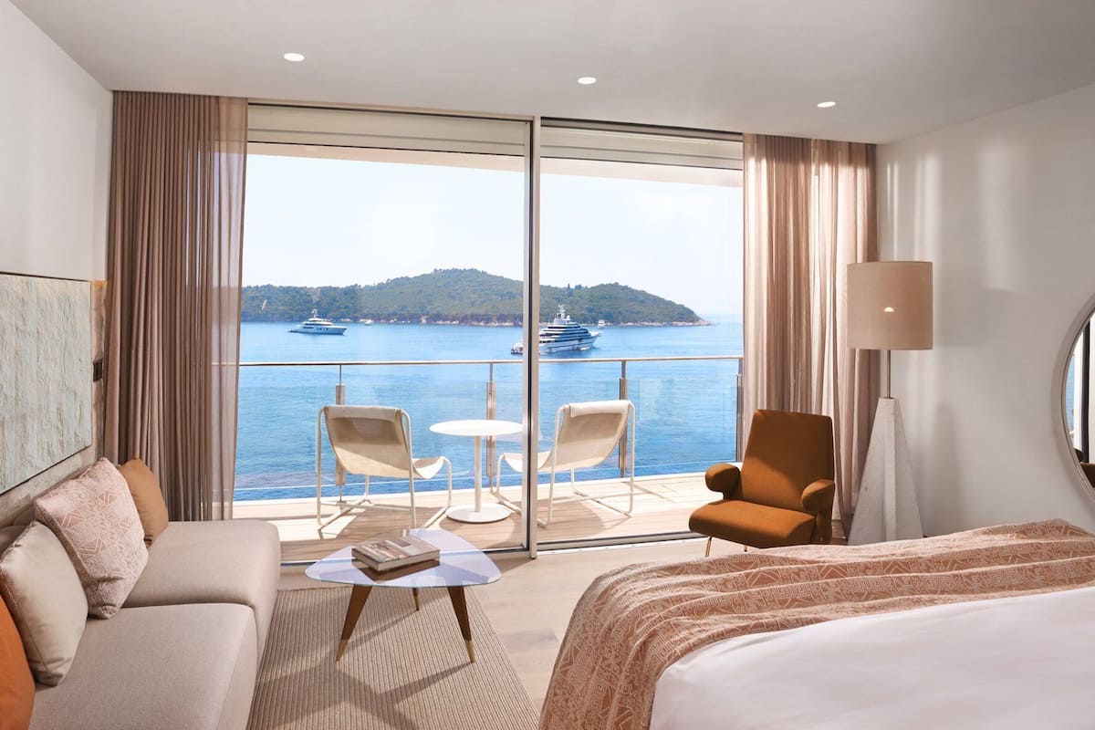 A hotel room with a balcony, a sofa, a chair, a small table, and a bed.