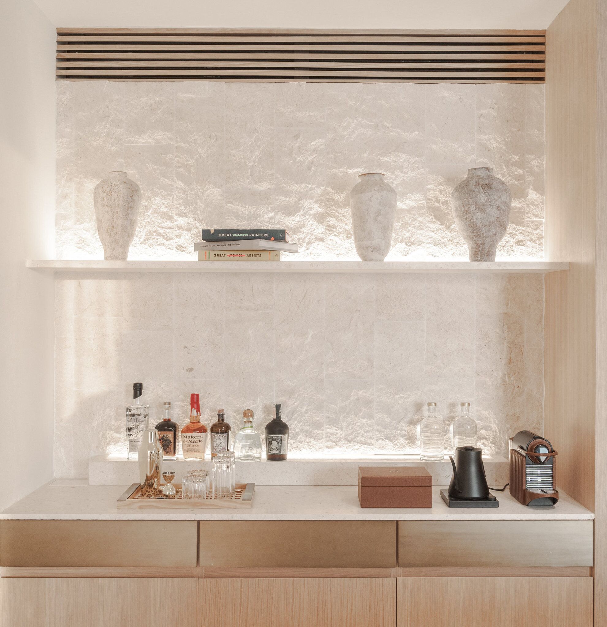 A shelf with books and vases, a countertop with bottles and a radio, and a window with a textured view.