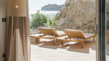 A hotel room with a bed, a large window, and a view of a rocky coastline.
