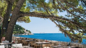 Un espace de restauration en plein air, avec des tables et des chaises, offrant une vue sur une étendue d’eau et un navire au loin.