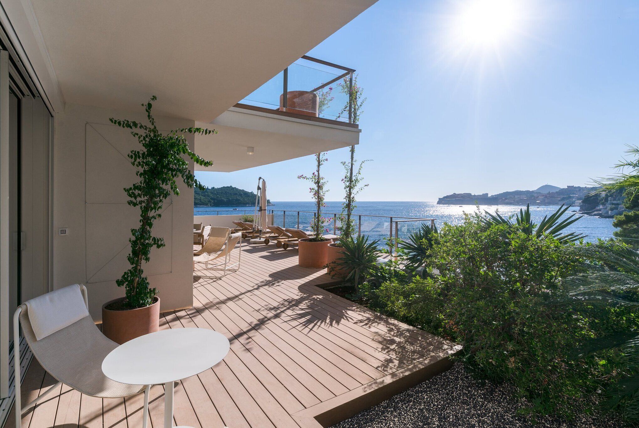 Una terrassa de fusta amb seients exteriors, plantes en testos i vista al mar.