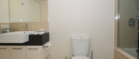 A bathroom with a white toilet, a sink with a black countertop, and a glass shower enclosure.