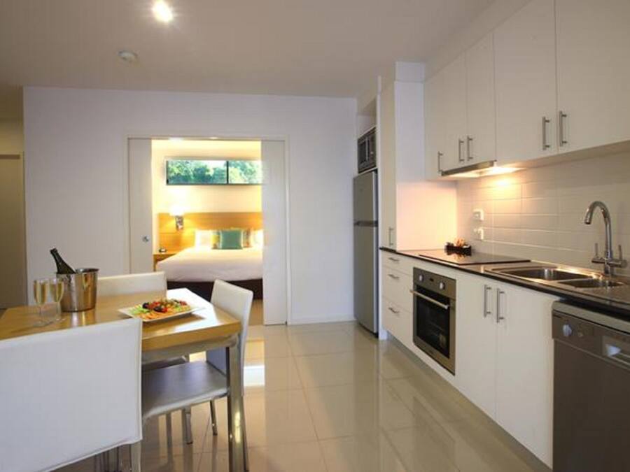Cocina moderna con gabinetes blancos, electrodomésticos de acero inoxidable y una zona de comedor con una mesa y sillas.